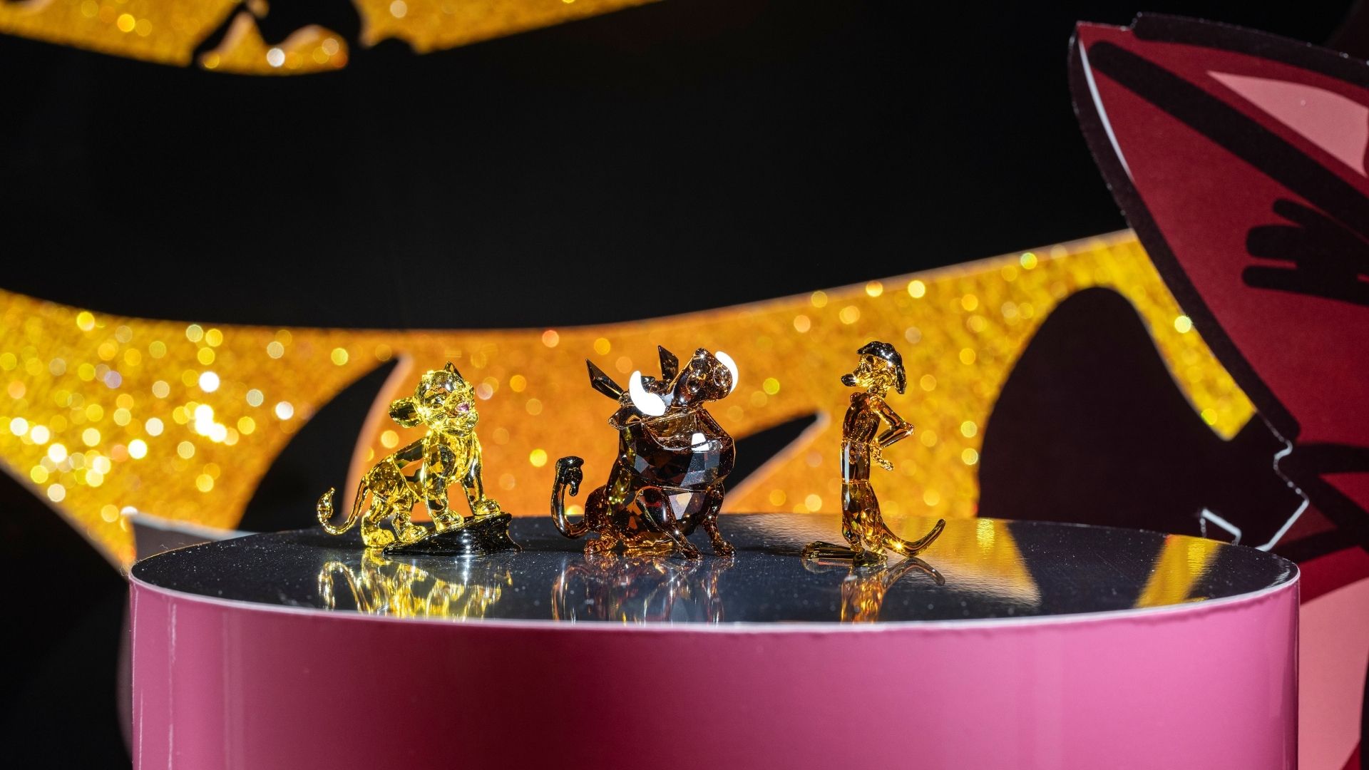 Disney x Swarovski art stage at Swarovski Kristallwelten Store Wattens — sparkling crystal figures of Simba, Timon and Pumbaa against a golden background.