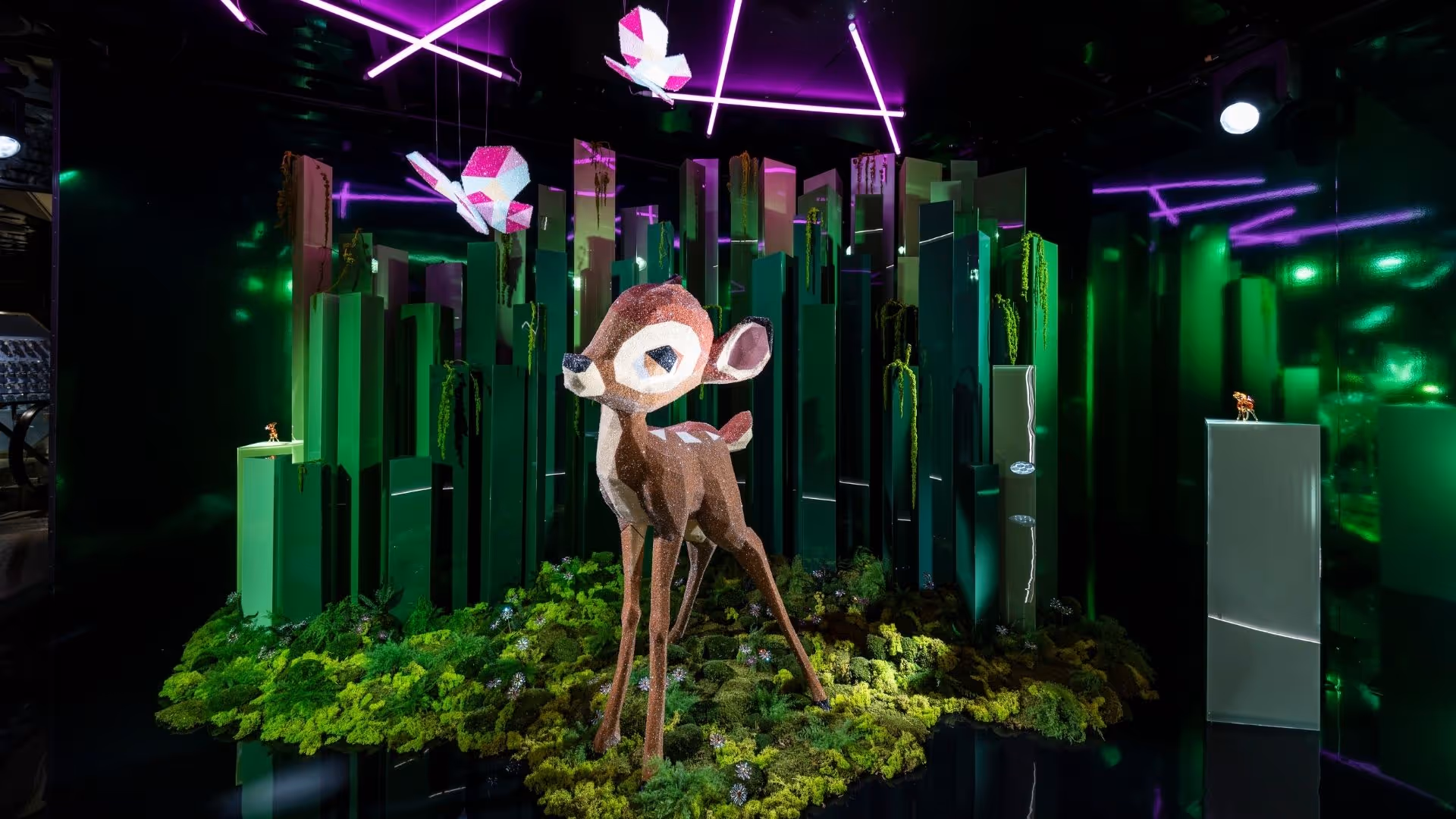 Kristallfigur von Disneys Bambi im Swarovski Kristallwelten Store Wien – kunstvolle Inszenierung mit funkelnden Kristallen, grüner Waldlandschaft, Lichteffekten und Kristallschmetterlingen.