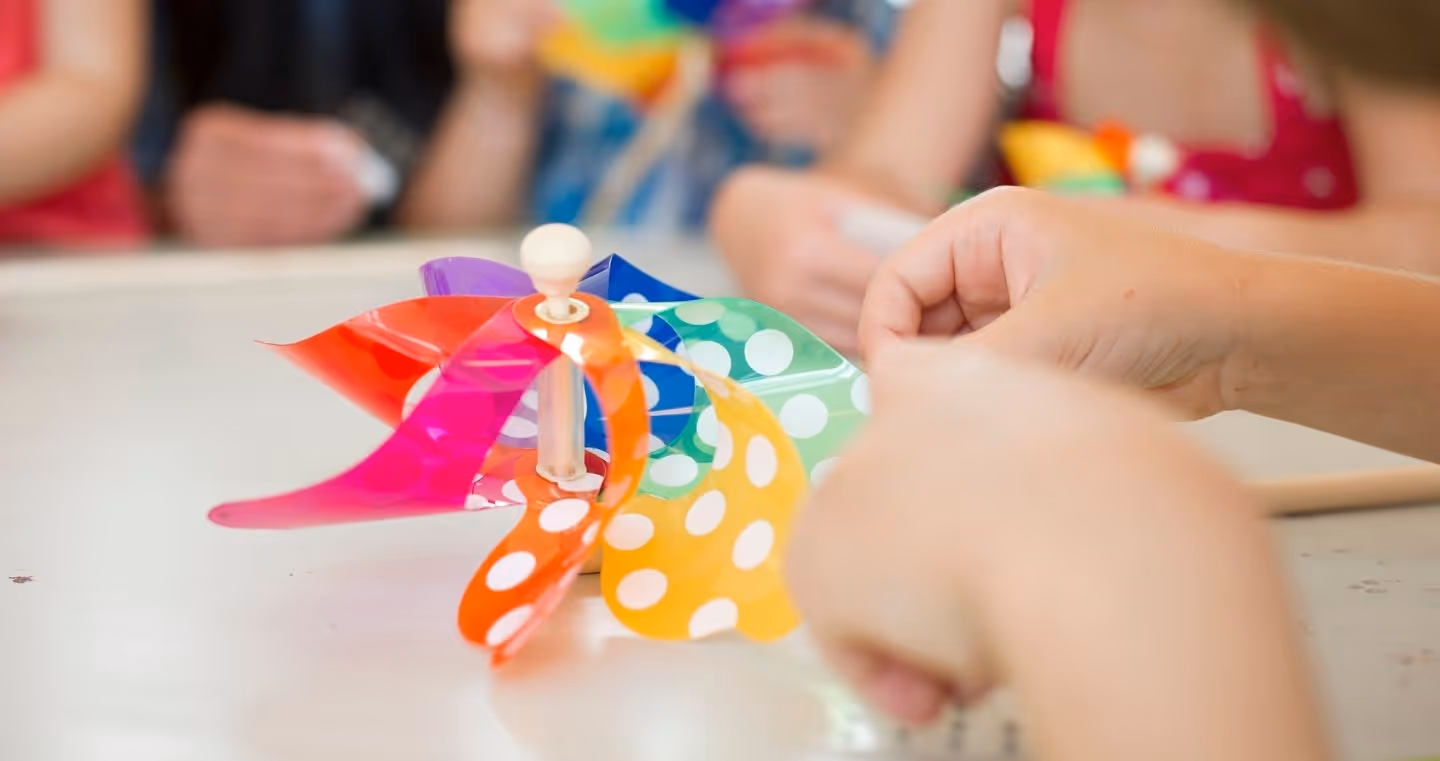 Kinderhände basteln ein buntes Windrad mit weißen Punkten während eines Kinderprogramms in den Swarovski Kristallwelten.