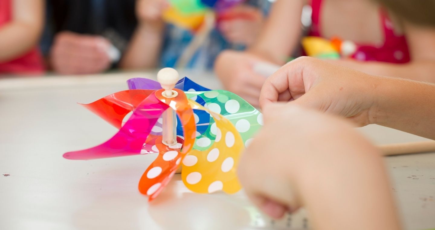 Kinderhände basteln ein buntes Windrad mit weißen Punkten während eines Kinderprogramms in den Swarovski Kristallwelten.