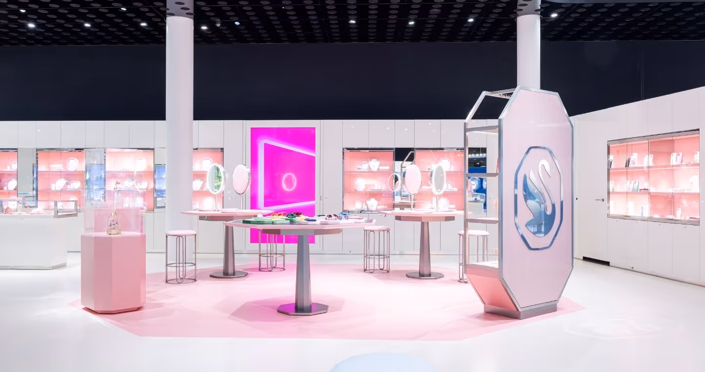 Innenansicht des Swarovski Kristallwelten Stores in Wattens: moderne Verkaufsfläche mit weißen Möbeln, rosa Akzenten, leuchtenden Präsentationsinseln und Vitrinen voller Schmuckstücke.