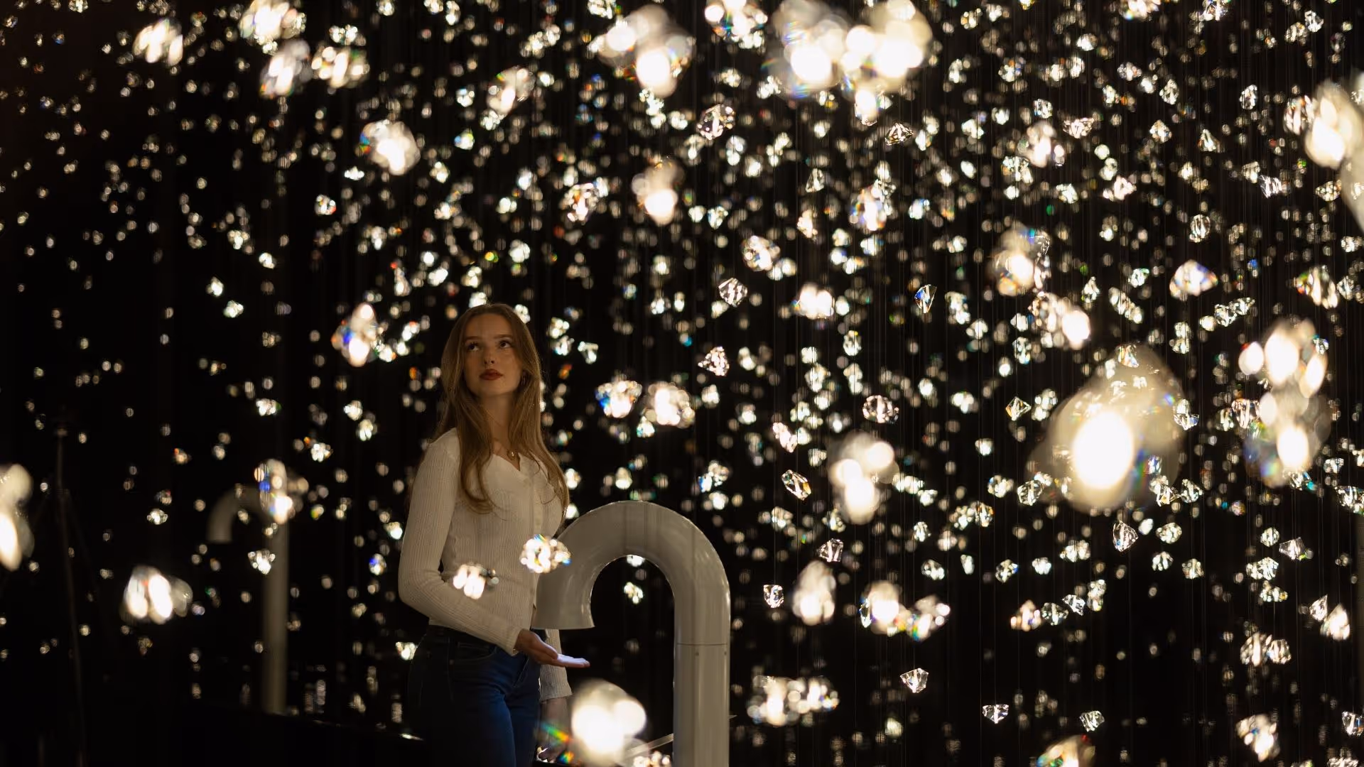 Eine junge Frau steht in der immersiven Wunderkammer Pulse Voronoi, umgeben von tausenden funkelnden Kristallen in den Swarovski Kristallwelten.