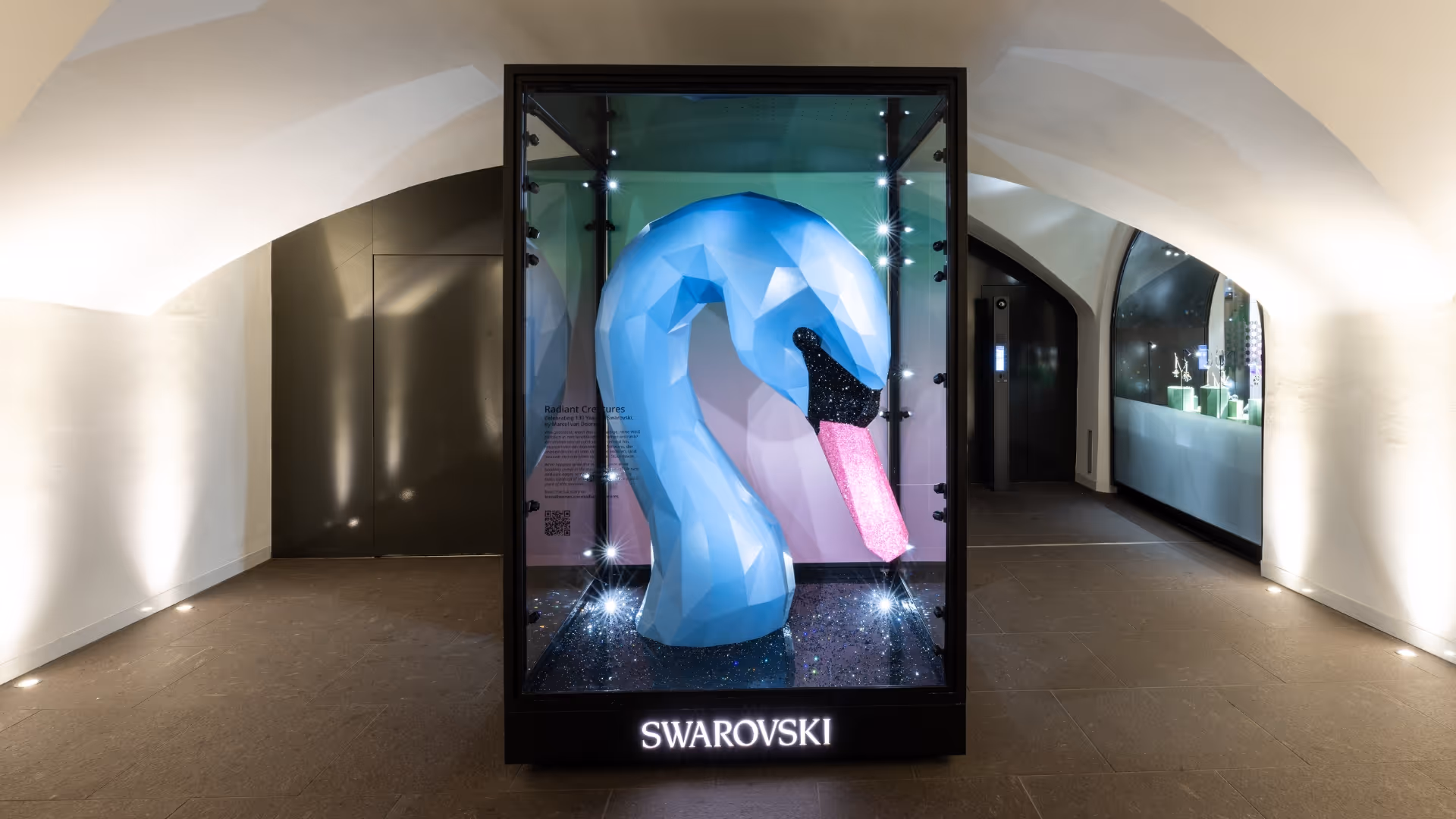 A larger-than-life crystal swan head in blue sits inside an outdoor store showcase. 