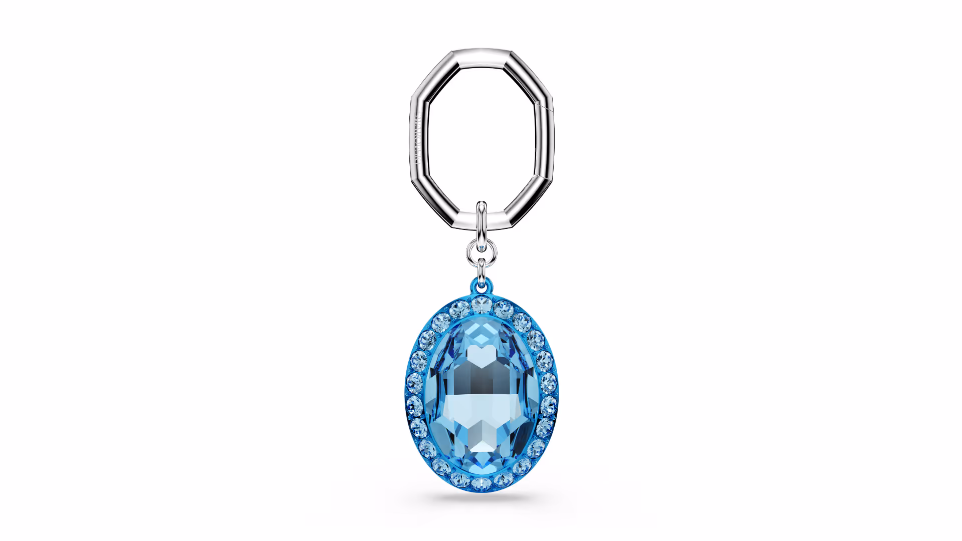 Elegant Swarovski key ring with a silver-coloured, octagonal carabiner ring. On it hangs an oval-cut, light blue crystal, surrounded by small, sparkling crystals in a matching shade of blue. Excerpted against a white background, focus on cut, color and richness of detail.