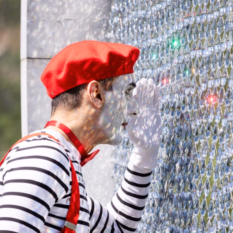 Pantomime mit roter Baskenmütze blickt durch funkelnde Kristalle im Park der Swarovski Kristallwelten.