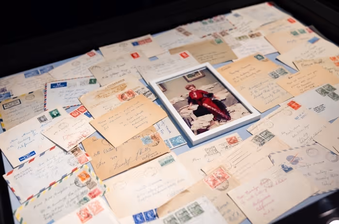 Sammlung alter Briefe und Postkarten mit Briefmarken, daneben gerahmtes Foto von Marilyn Monroe in rotem Outfit auf einem Tisch.