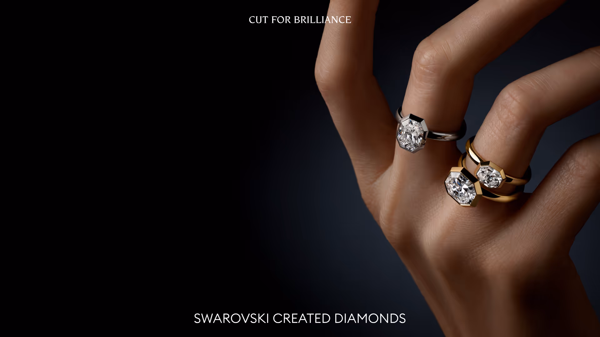 Drei Swarovski Created Diamond Ringe an einer Hand vor dunklem Hintergrund.