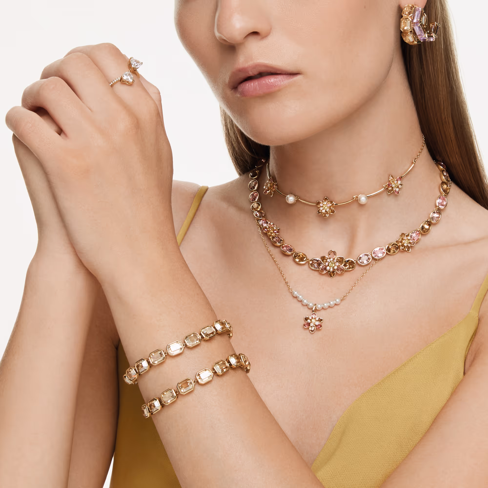 Elegant jewelry shot with multiple Swarovski necklaces, bracelets and earrings with crystals, presented on a person against a light background.