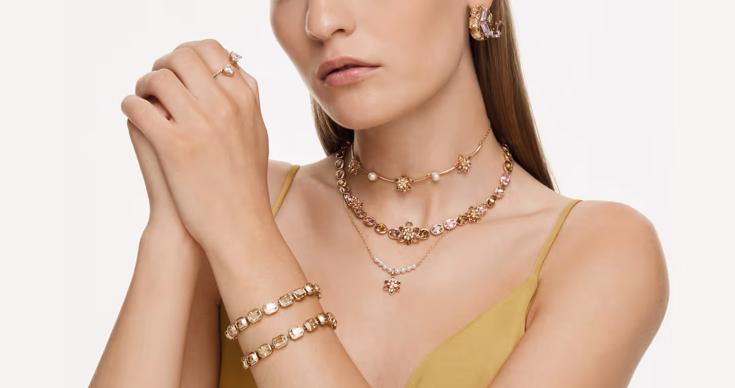 Elegant jewelry shot with multiple Swarovski necklaces, bracelets and earrings with crystals, presented on a person against a light background.