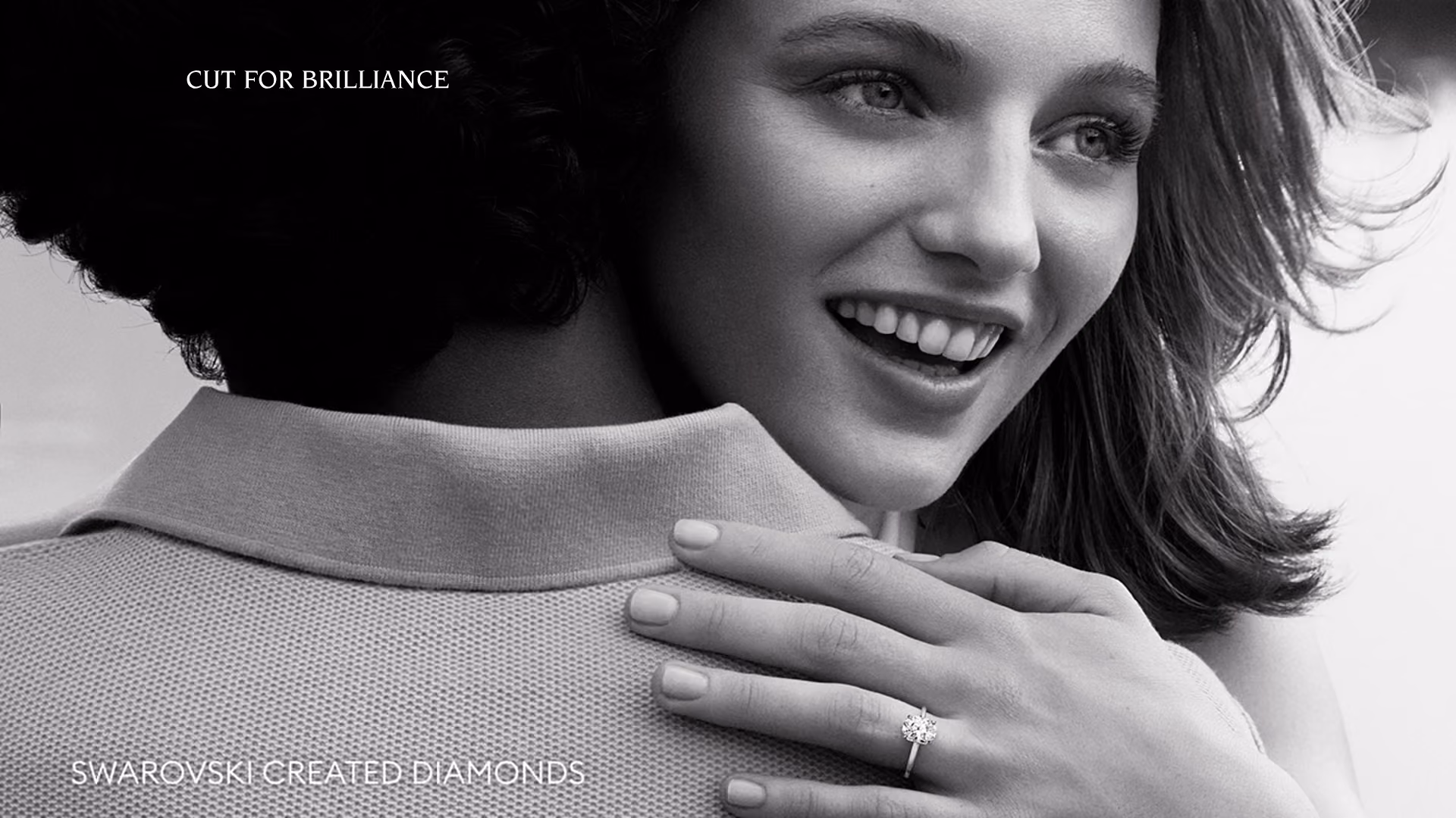 A person wears a Swarovski Created Diamonds ring and places their hand on another person's shoulder. Elegant black and white shot with “Cut for Brilliance.”