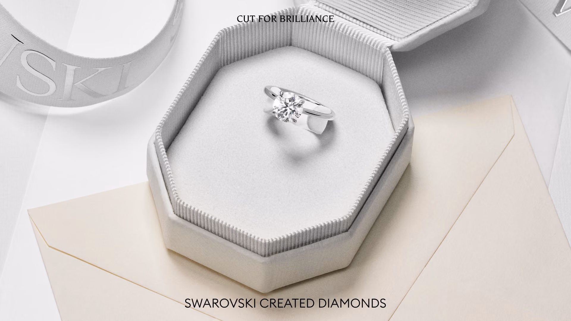 Ring with diamond in an opened jewelry box on a light background. In addition, “Cut for Brilliance,” including Swarovski Created Diamonds.