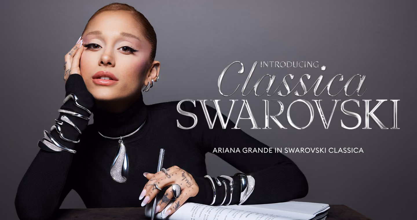 Person wearing a black turtleneck sweater with silver-colored Swarovski jewelry on arms and neck against a grey background.