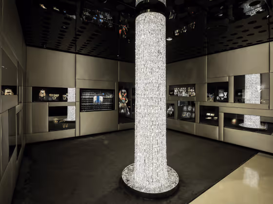 Moderner Raum mit klaren Linien von Vincent Van Duysen: Ein leuchtender Kristallpfeiler in der Mitte des Raumes, umgeben von dunklen Vitrinen mit Schmuck und Kristallobjekten.