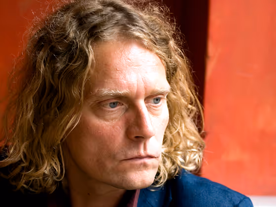 Michael Kienzer, österreichischer Künstler, 2006 im Porträt mit lockigen Haaren, vor neutralem Hintergrund.