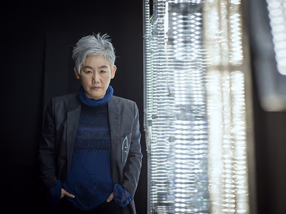 Lee Bul, südkoreanische Künstlerin, 2015 im Porträt mit grauen Haaren und blauer Kleidung, ernst in die Kamera blickend.