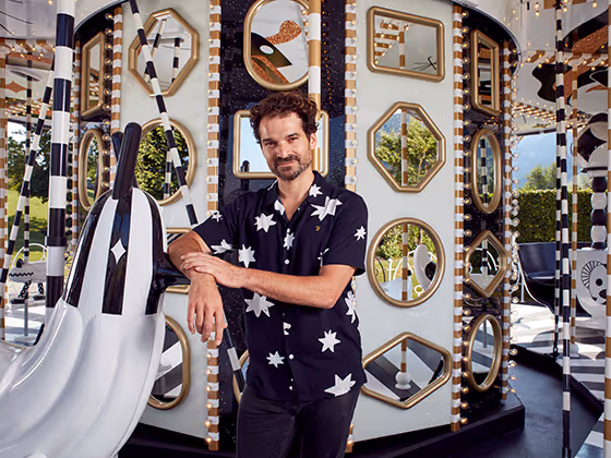 Jaime Hayon, spanischer Designer, 2019 in auffälliger Sternenbluse, lachend vor seiner Karussell-Installation.