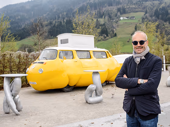 Erwin Wurm, österreichischer Künstler, 2017 mit Sonnenbrille und Schal, posierend vor seiner Installation "Dicker Bus"