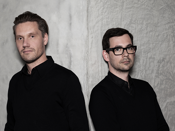 Fredrikson Stallard, britisches Designerduo, 2012 im Porträt, beide in schwarzer Kleidung vor hellem Hintergrund.
