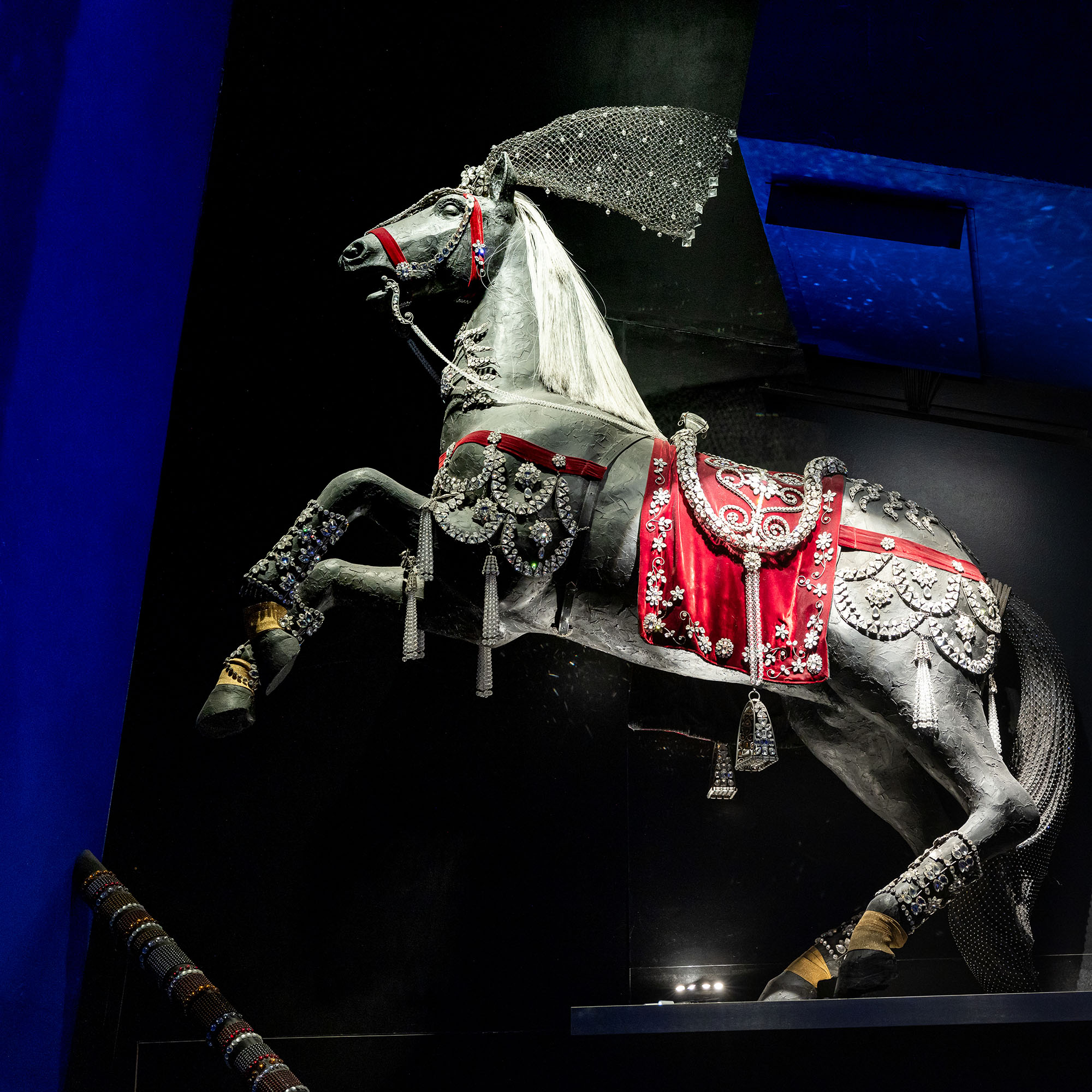 Ein detailreich dekoriertes Pferd von Philippe Ferrandis, verziert mit funkelnden Swarovski-Kristallen und roten Ornamenten. Das Pferd steht aufrecht auf den Hinterbeinen und wirkt majestätisch.