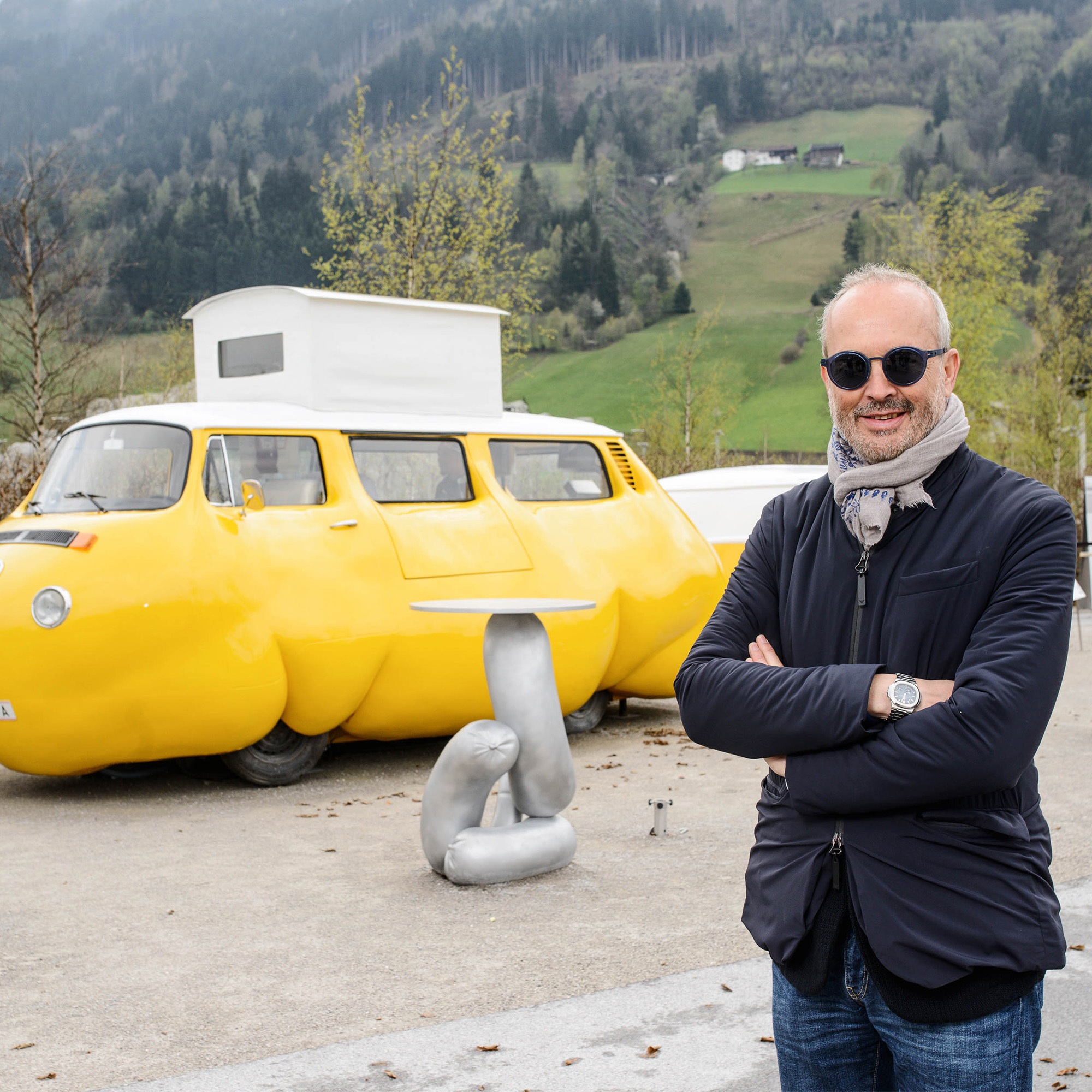 Erwin Wurm, österreichischer Künstler, 2017 mit Sonnenbrille und Schal, posierend vor seiner Installation "Dicker Bus"