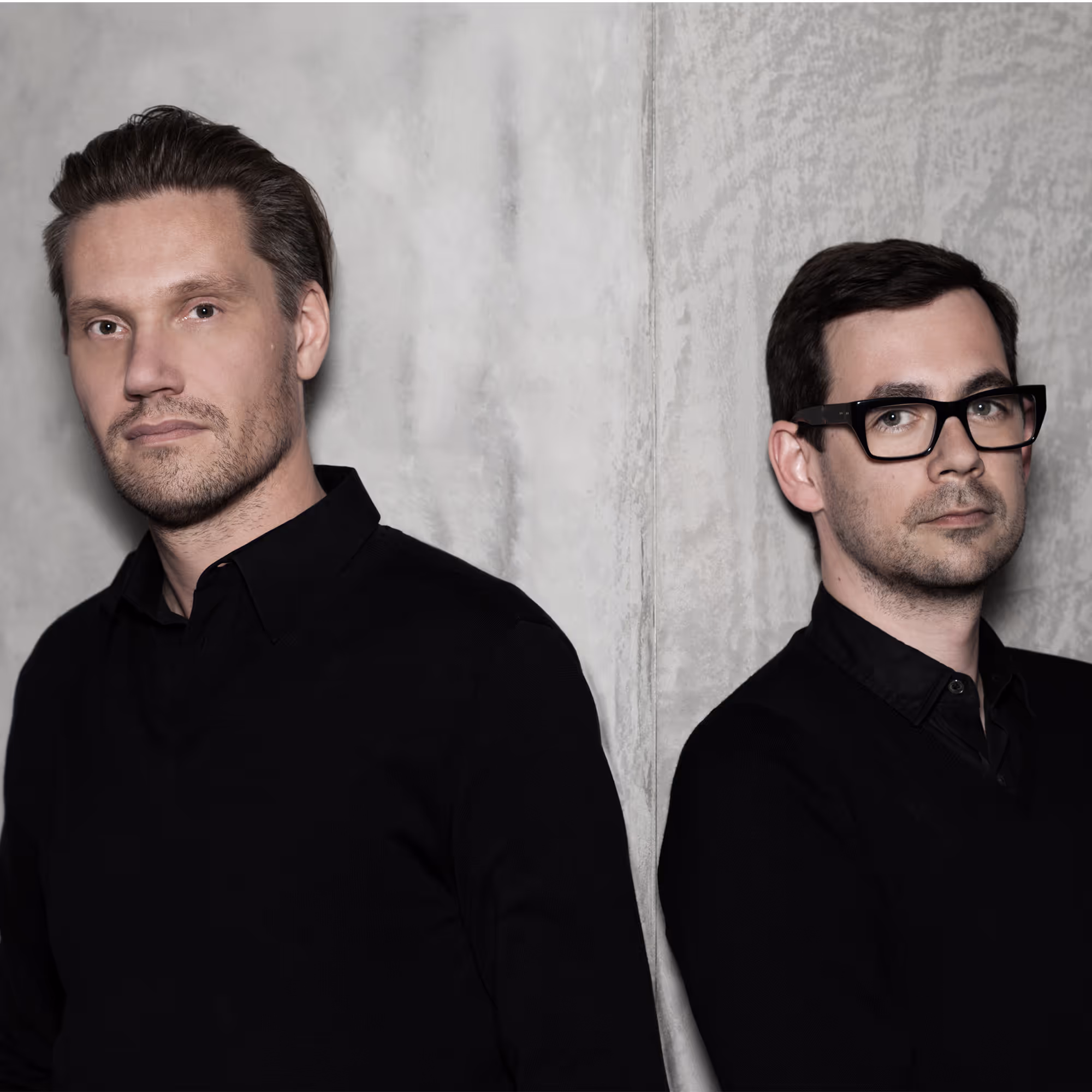 Fredrikson Stallard, britisches Designerduo, 2012 im Porträt, beide in schwarzer Kleidung vor hellem Hintergrund.