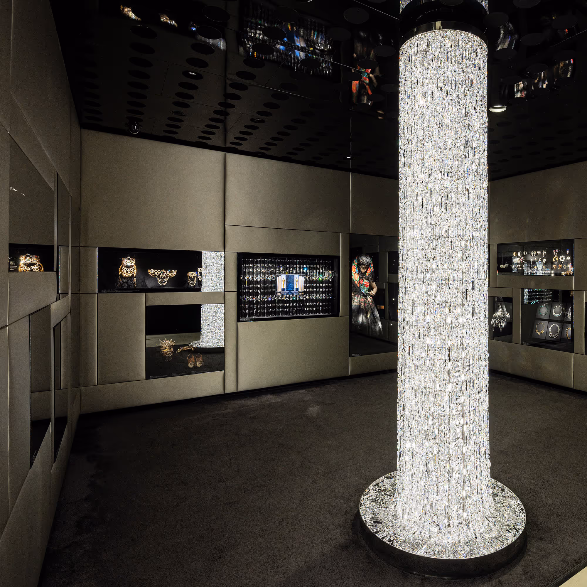 Moderner Raum mit klaren Linien von Vincent Van Duysen: Ein leuchtender Kristallpfeiler in der Mitte des Raumes, umgeben von dunklen Vitrinen mit Schmuck und Kristallobjekten.