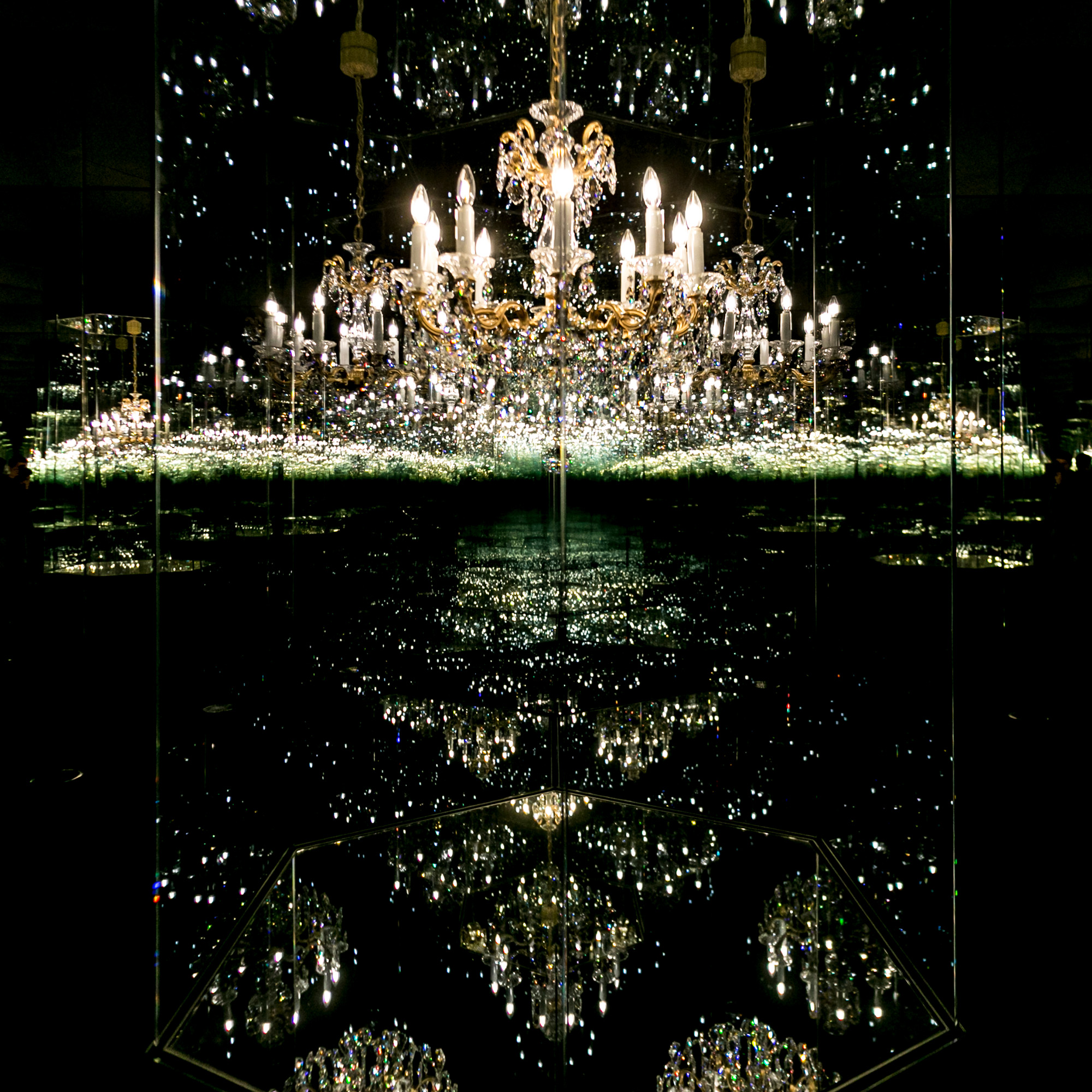 Kunstwerk 'Chandelier of Grief': Ein Kristallluster in einem Spiegelraum, der durch Reflexionen endlos erscheint.