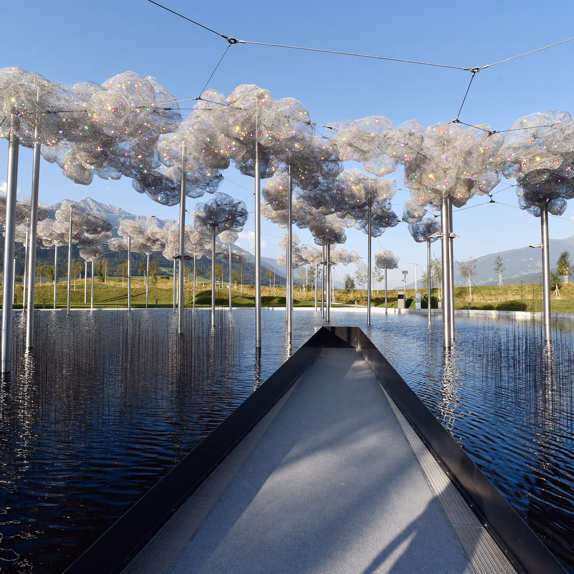 Installation 'Kristallwolke': Tausende funkelnde Kristalle hängen über einem dunklen Wasserbecken und spiegeln sich.