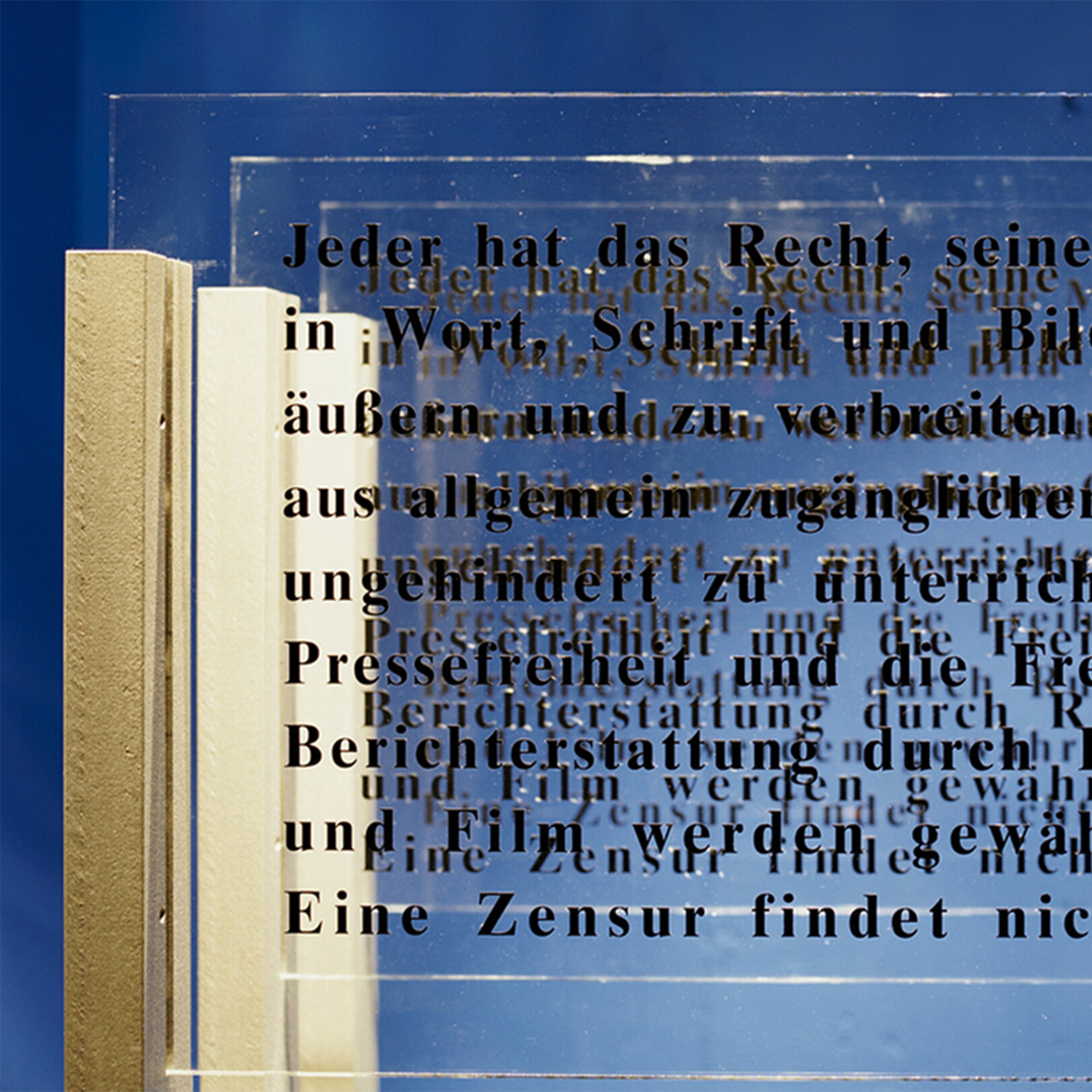 Installation 'Augentrost': Transparente Glasplatten mit schwarzen Buchstaben, die Texte zu Freiheit und Menschenrechten zeigen, künstlerisch beleuchtet.