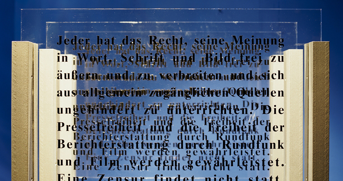 Installation 'Augentrost': Transparente Glasplatten mit schwarzen Buchstaben, die Texte zu Freiheit und Menschenrechten zeigen, künstlerisch beleuchtet.