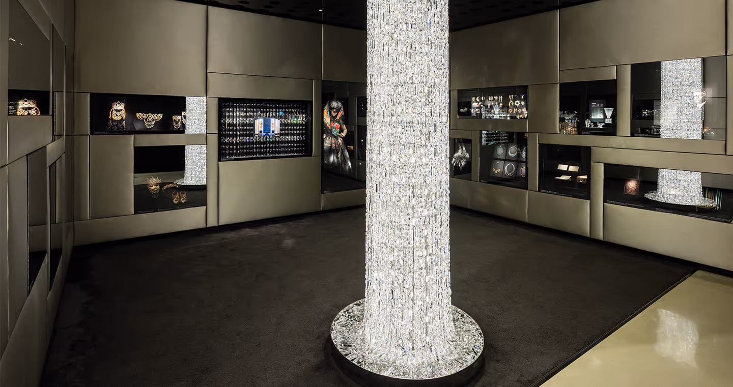 Moderner Raum mit klaren Linien von Vincent Van Duysen: Ein leuchtender Kristallpfeiler in der Mitte des Raumes, umgeben von dunklen Vitrinen mit Schmuck und Kristallobjekten.