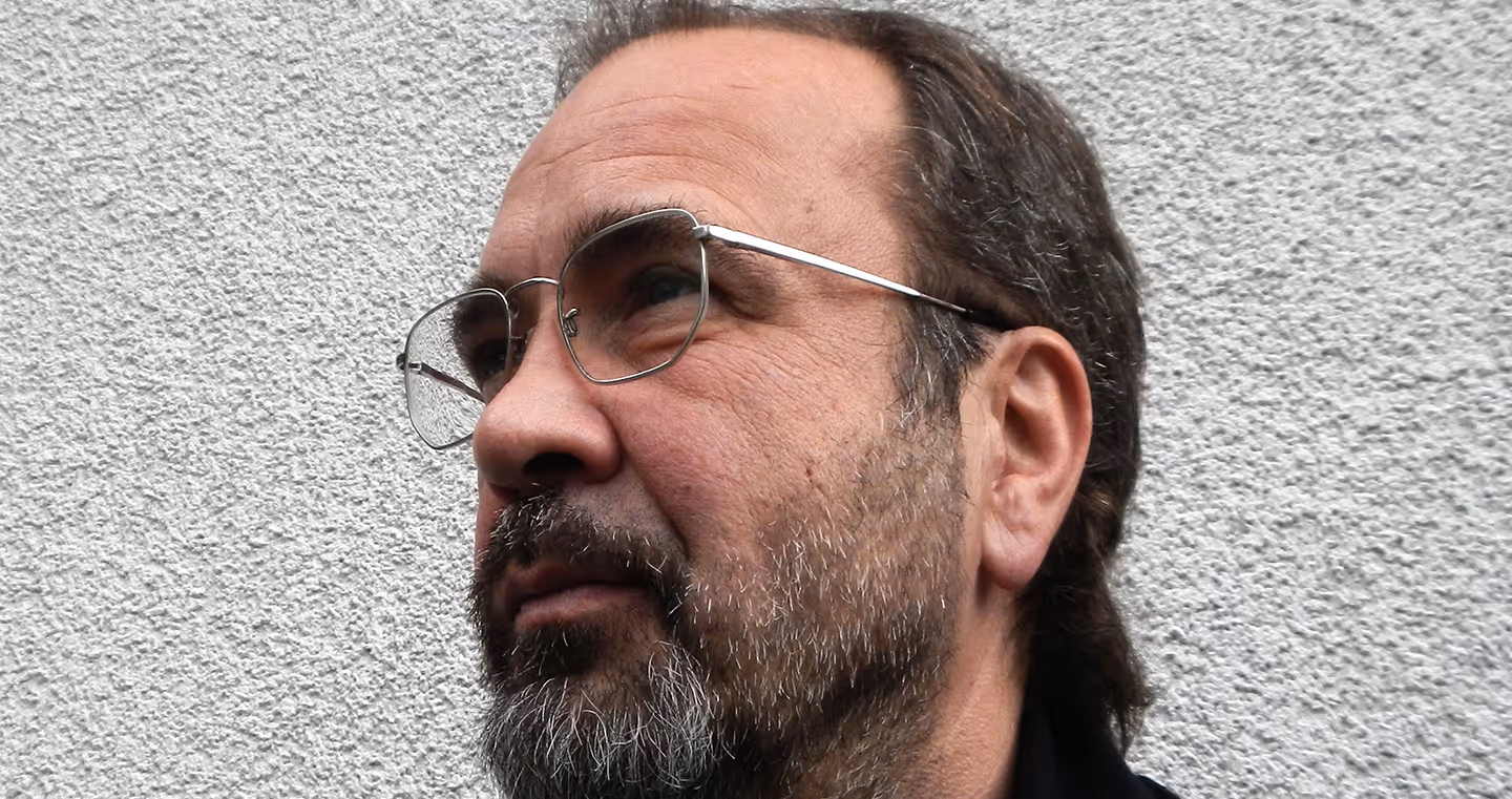 Martin Gostner, österreichischer Künstler, 2014 im Porträt mit grauem Hintergrund, ernster Gesichtsausdruck.