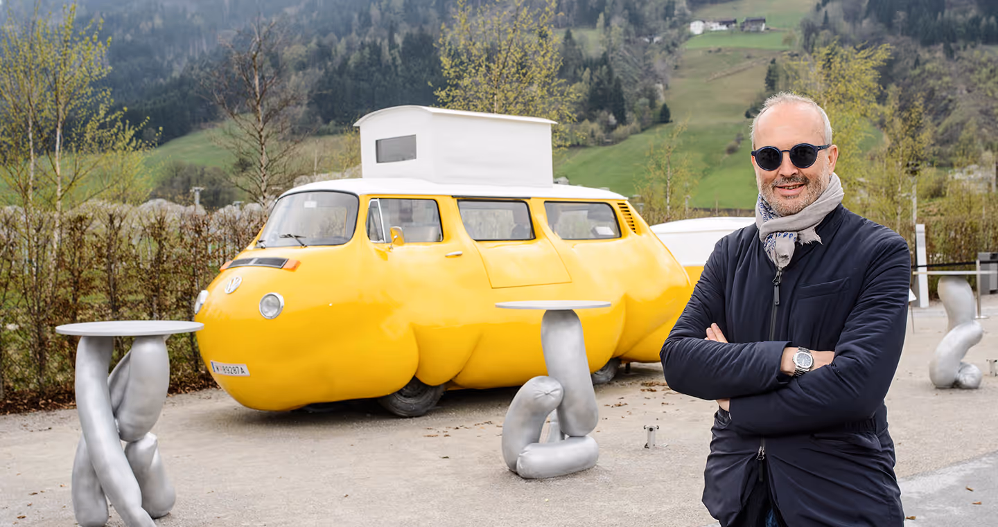 Erwin Wurm, österreichischer Künstler, 2017 mit Sonnenbrille und Schal, posierend vor seiner Installation "Dicker Bus"