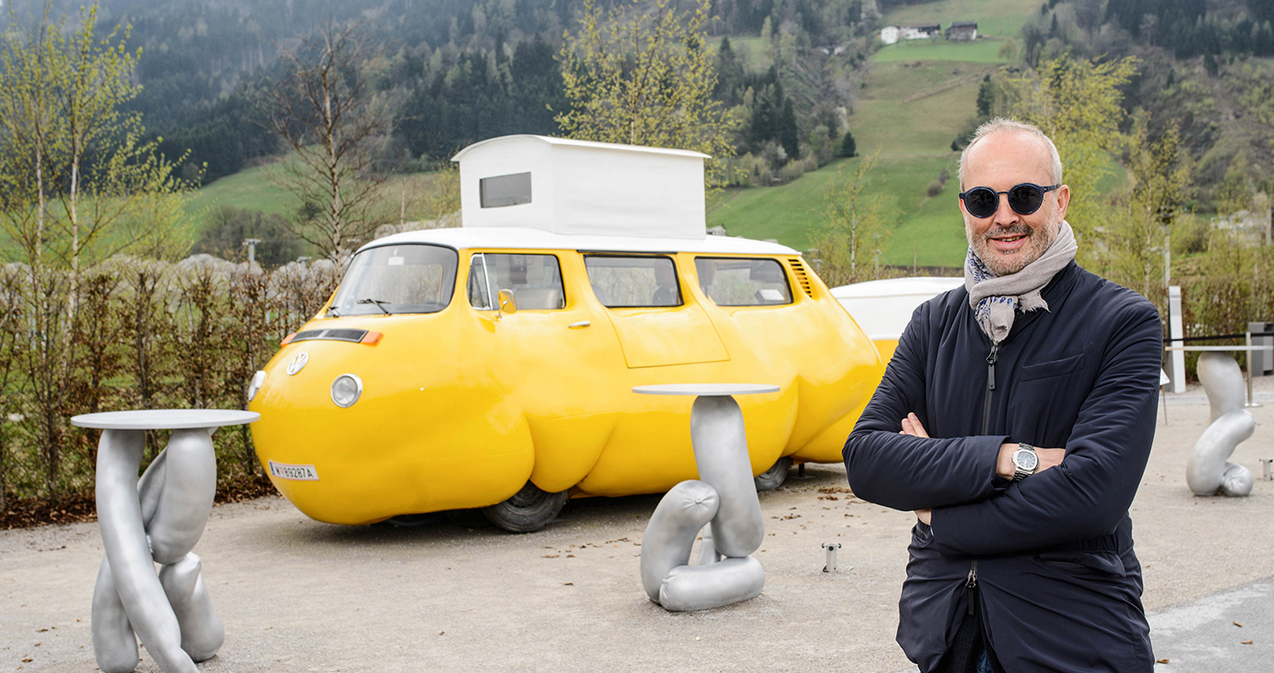 Erwin Wurm, österreichischer Künstler, 2017 mit Sonnenbrille und Schal, posierend vor seiner Installation "Dicker Bus"
