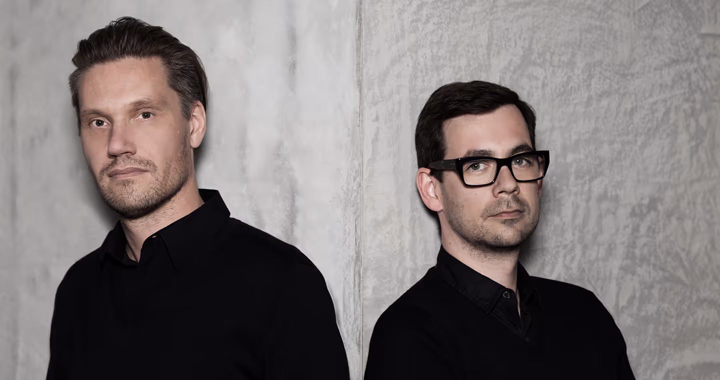 Fredrikson Stallard, britisches Designerduo, 2012 im Porträt, beide in schwarzer Kleidung vor hellem Hintergrund.