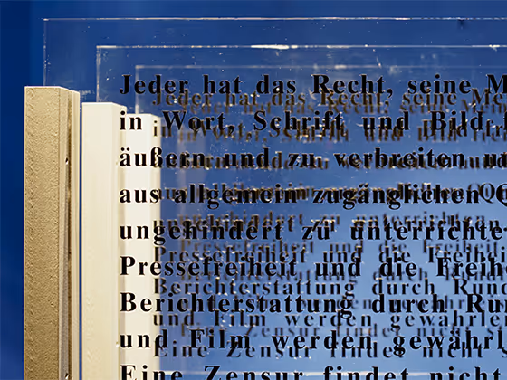 Installation 'Augentrost': Transparente Glasplatten mit schwarzen Buchstaben, die Texte zu Freiheit und Menschenrechten zeigen, künstlerisch beleuchtet.