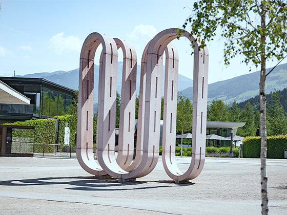 Kunstwerk 'Conveyor Belt': Große rosafarbene Skulptur im Freien, bestehend aus geschwungenen, organischen Formen.