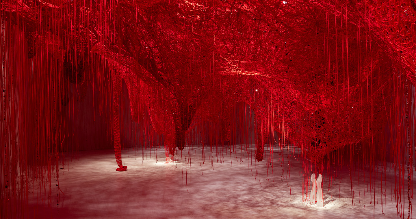 Rauminstallation 'Crystallizing Identity': Hunderte rote Fäden spannen sich durch den Raum und erzeugen ein dichtes Netz aus Licht und Schatten.