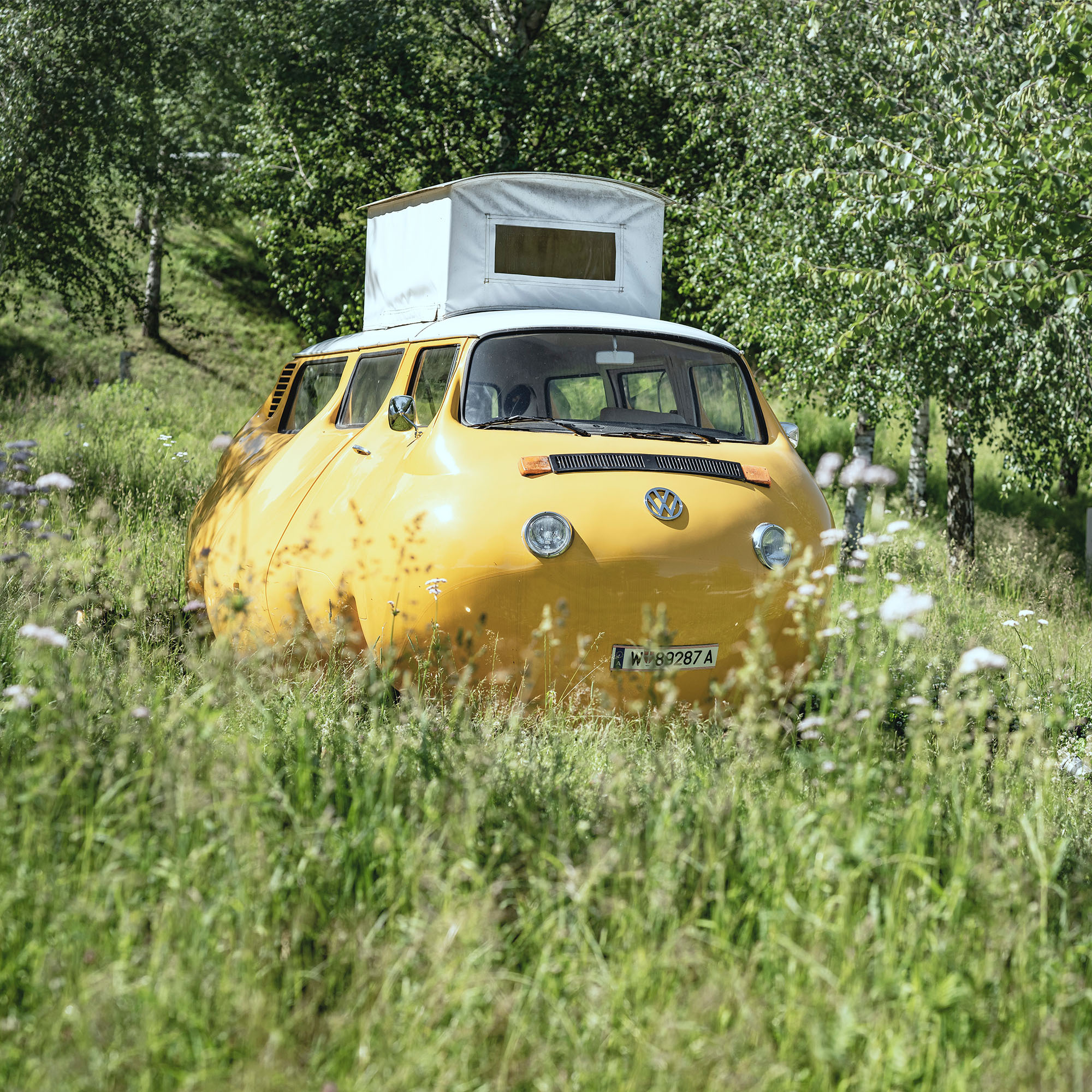 Skulptur 'Dicker Bus': Ein verzerrt wirkender, bauchiger Bus in Grau, humorvoll inszeniert.