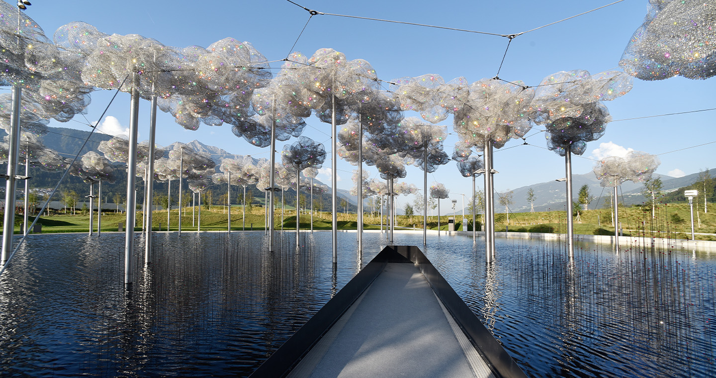 Installation 'Kristallwolke': Tausende funkelnde Kristalle hängen über einem dunklen Wasserbecken und spiegeln sich.