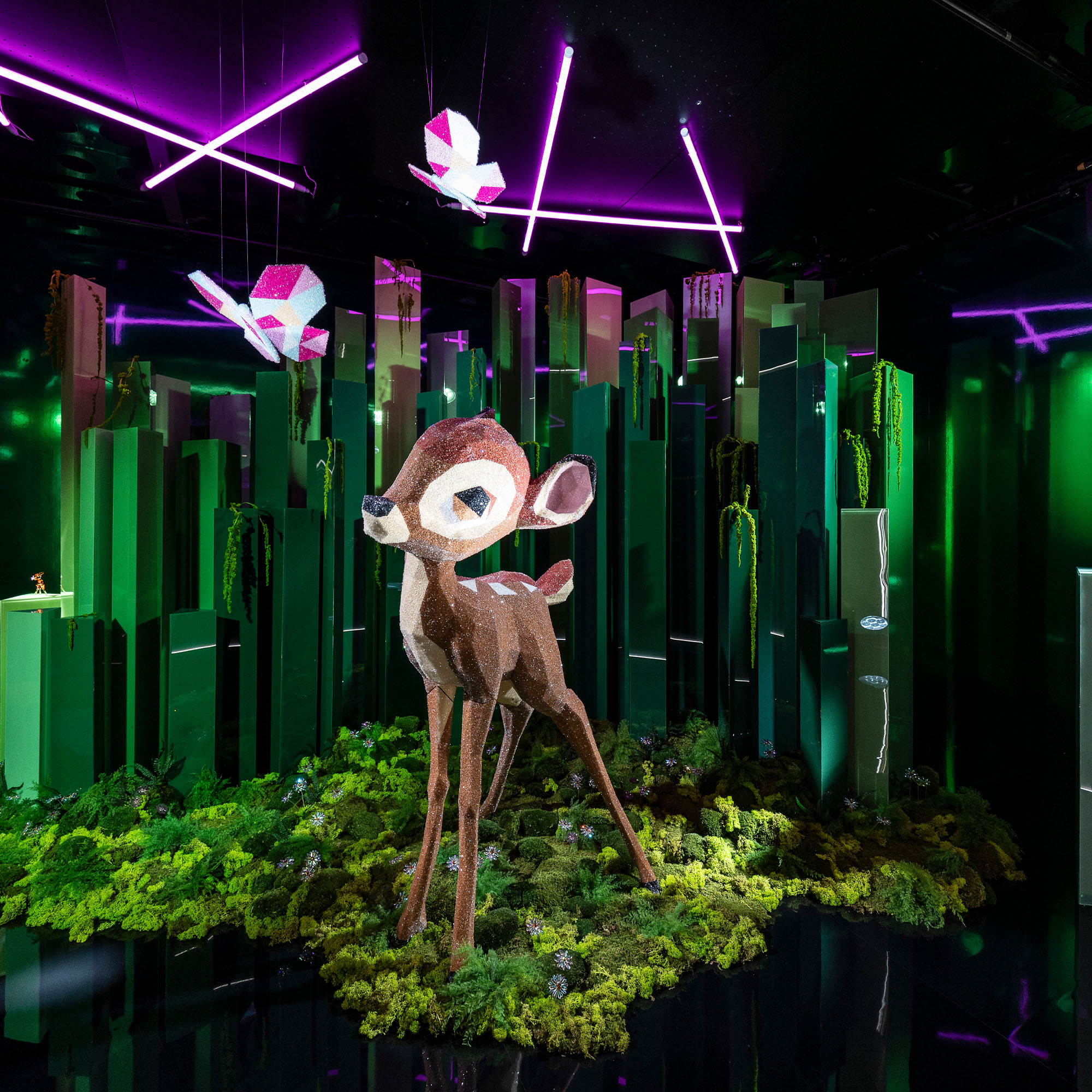 Kristallisiertes Bambi in einem Schaufenster, im Hintergrund grüne Stelen welche einen Wald darstellen sollen.