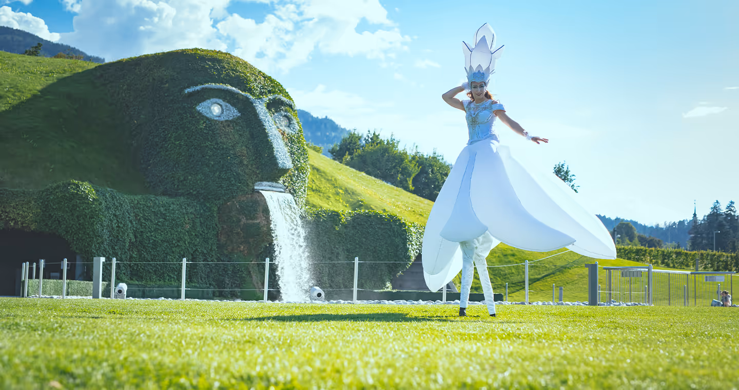 Eine Stelzengeherin in einem weißen Kleid vor den Swarovski Kristallwelten.