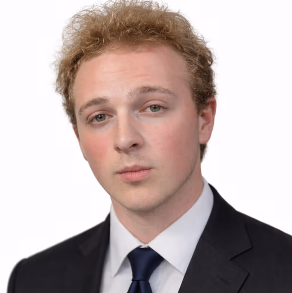 Portrait of Ryan. Curly dark blond man wearing a black suit, white shirt, and dark blue tie against a white background.