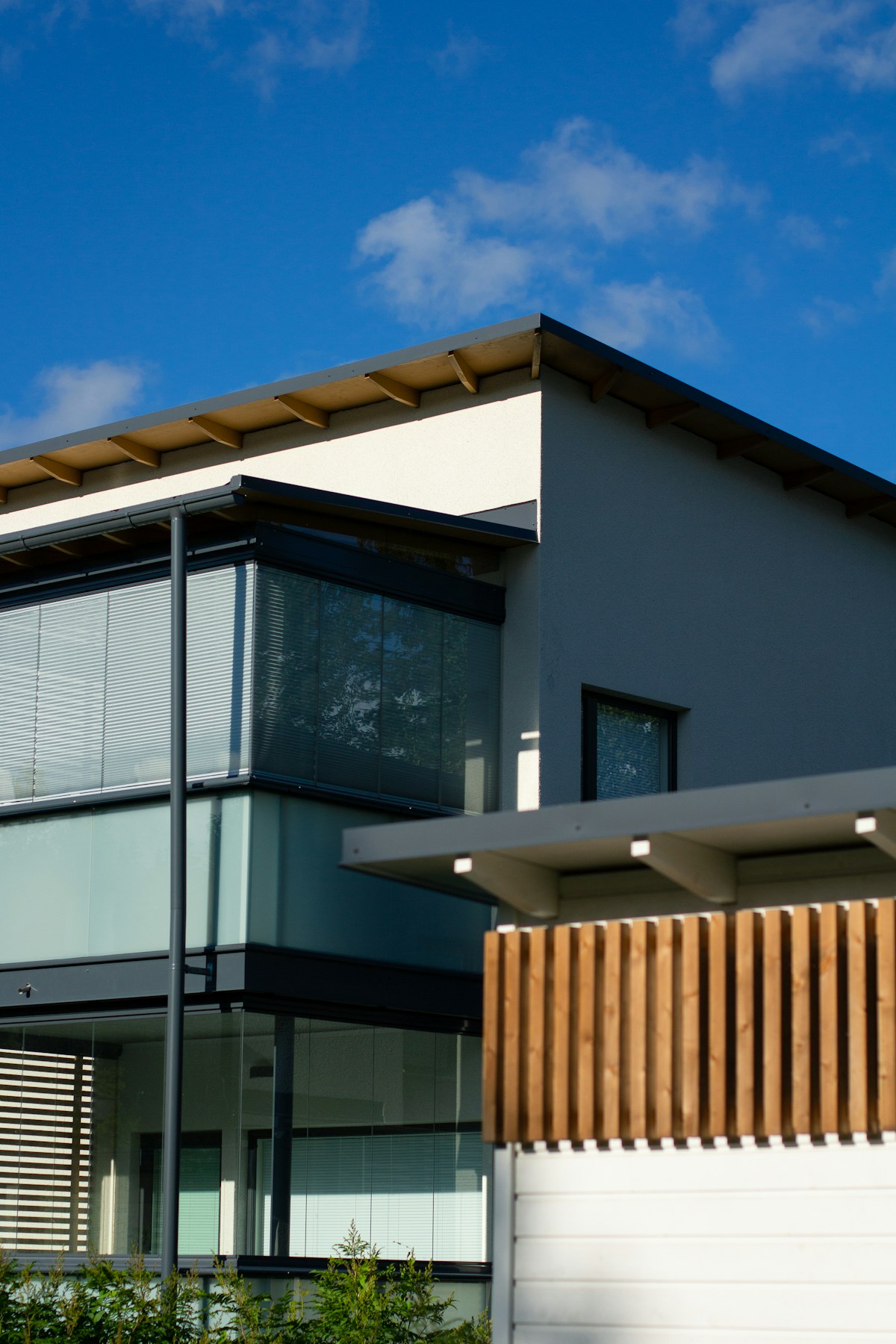 Modern residential facade with timber screens, glazing and a white roof