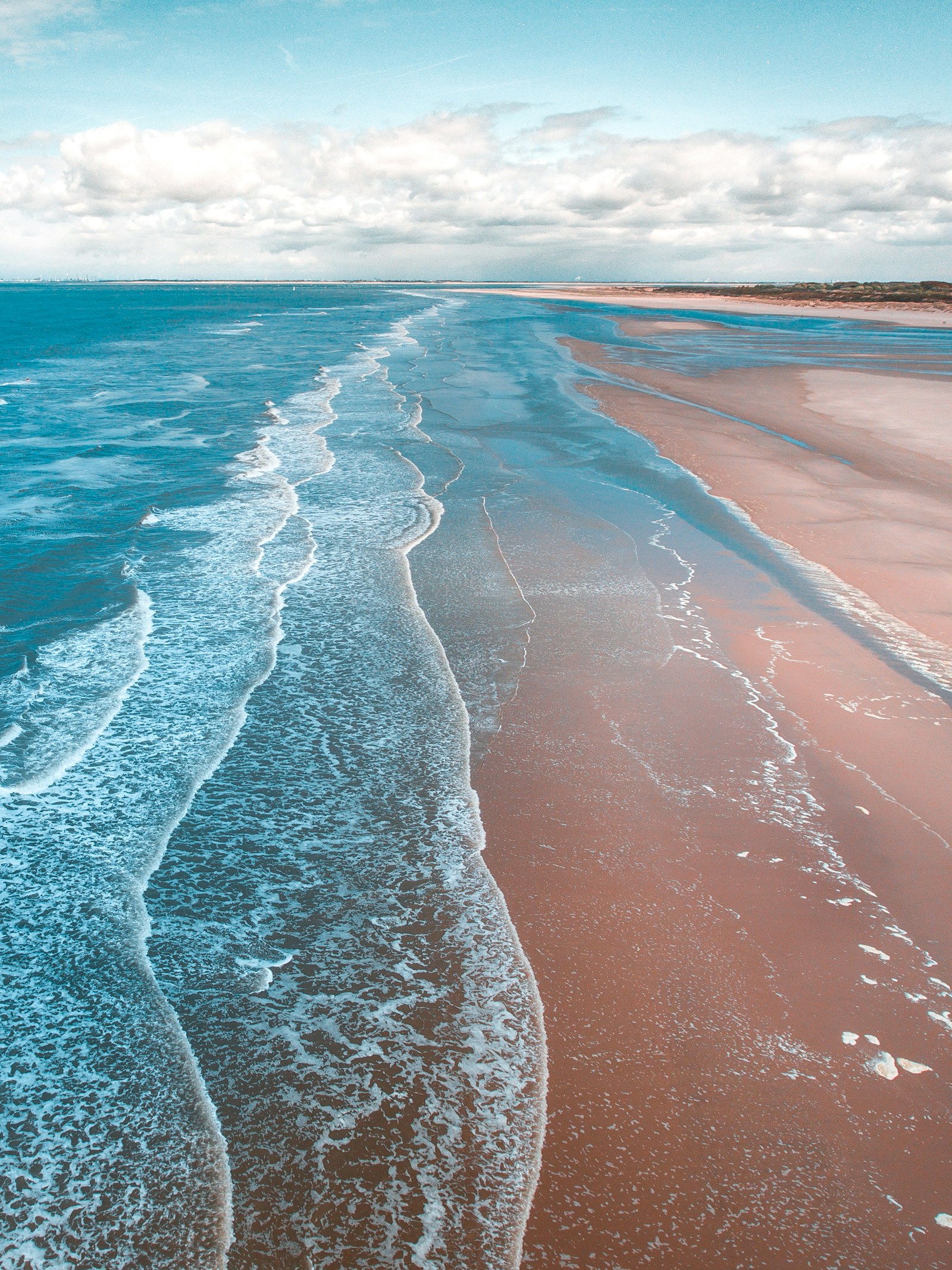 Turquoise waves breaking along an empty sandy shore