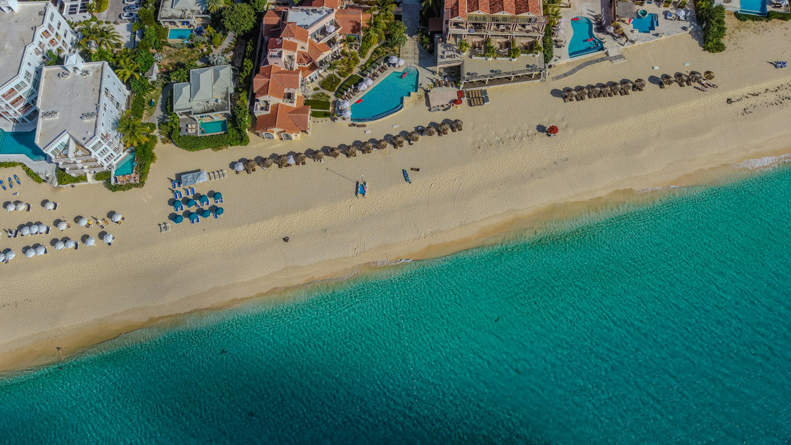Aerial view of a sandy coast beside buildings and turquoise water