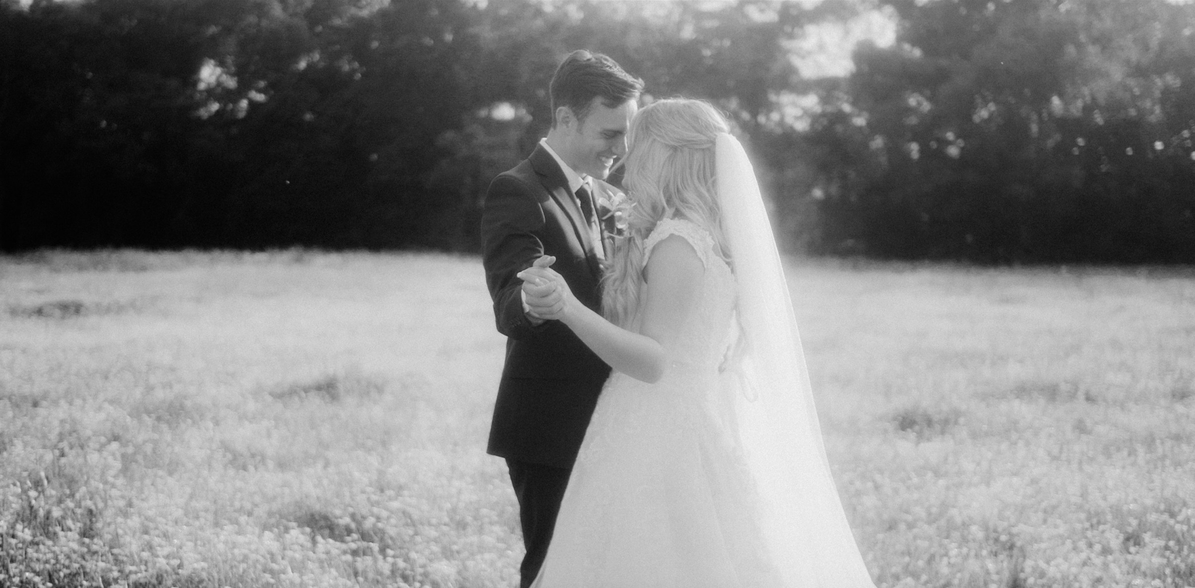 A couple in wedding attire standing together in a sunlit field