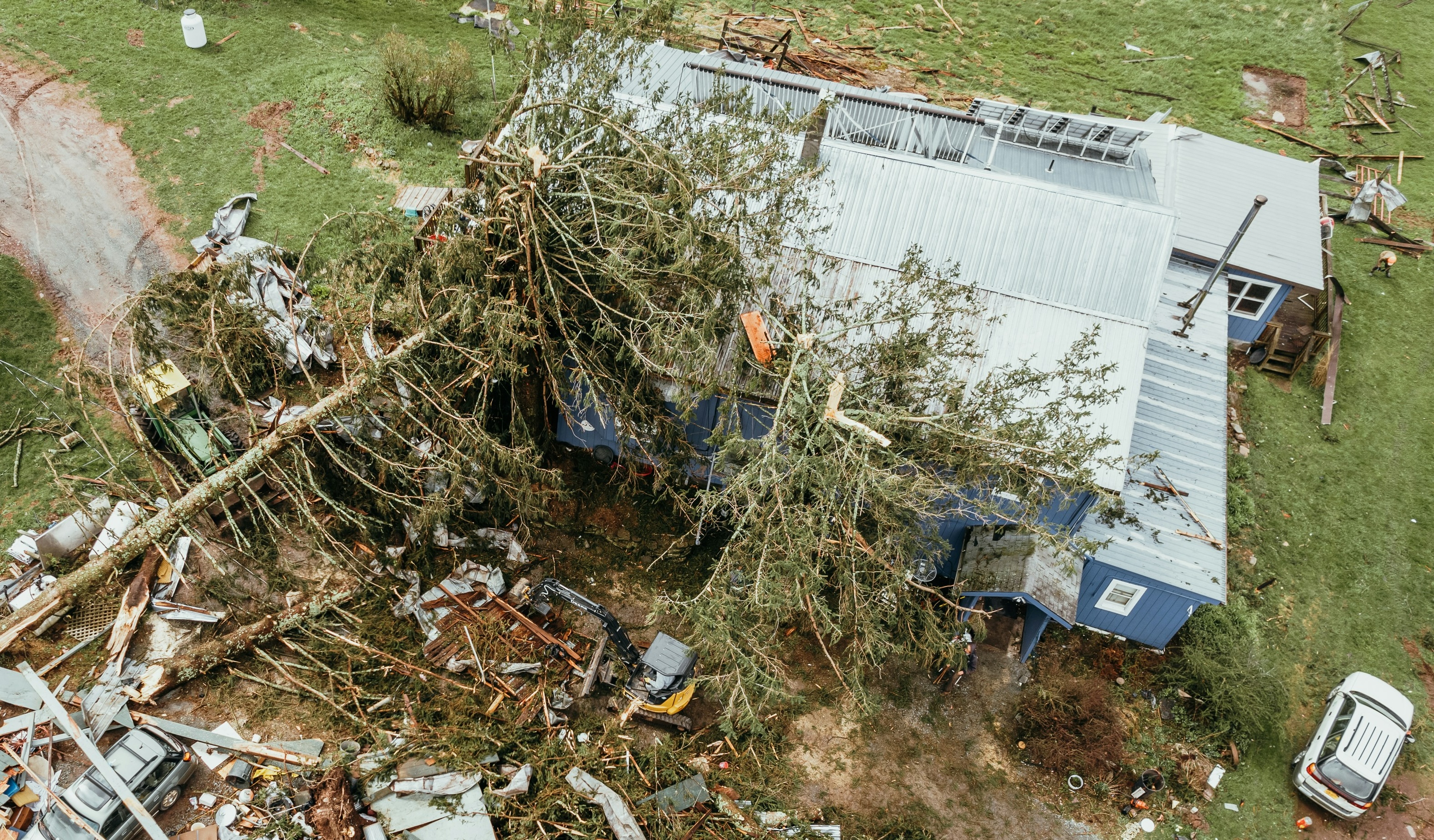 Aerial view of a Hurricane Helene-damaged South Carolina home with a fallen tree across the roof and storm debris in the yard