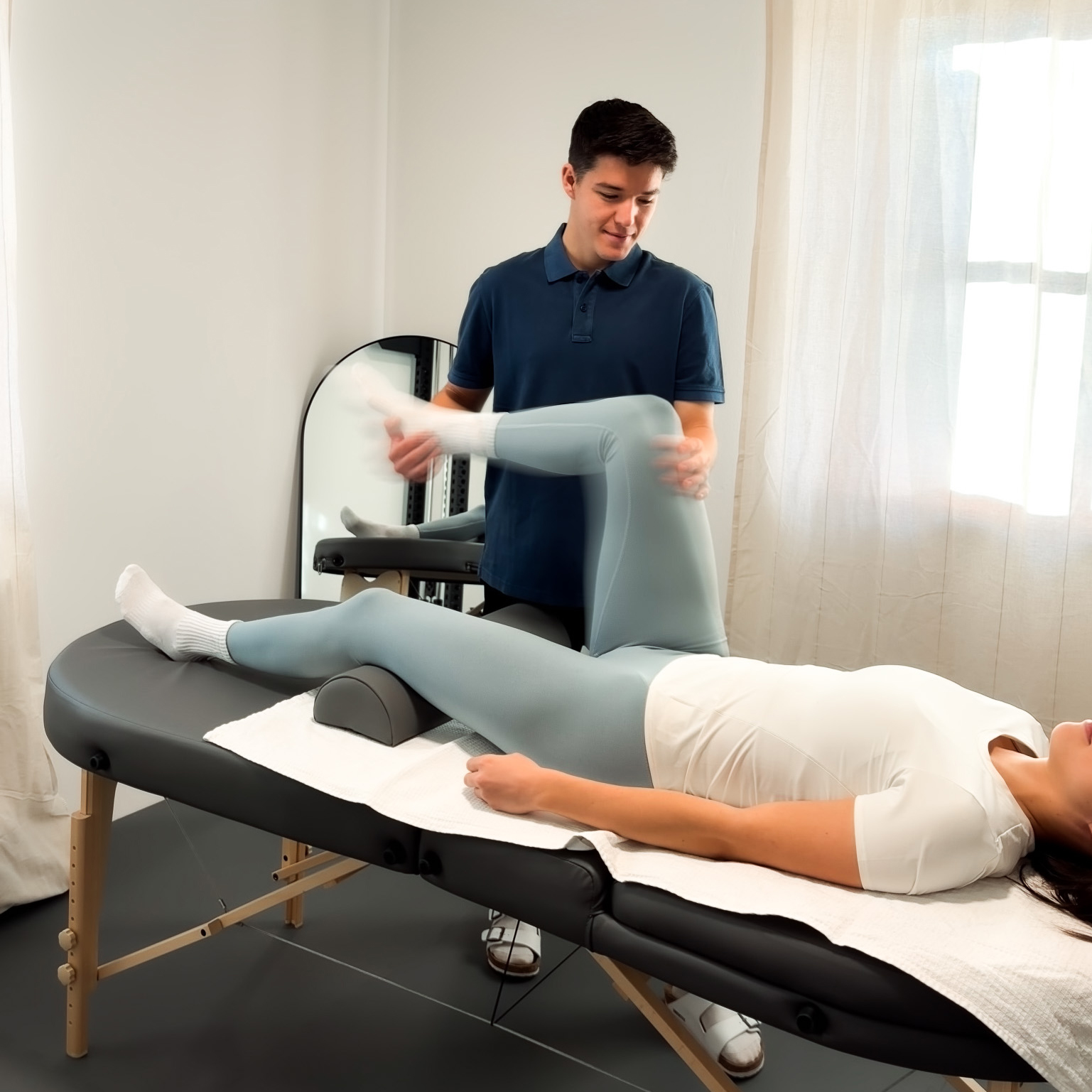 Physiotherapist assisting a woman with leg exercises on a treatment table in a bright room.