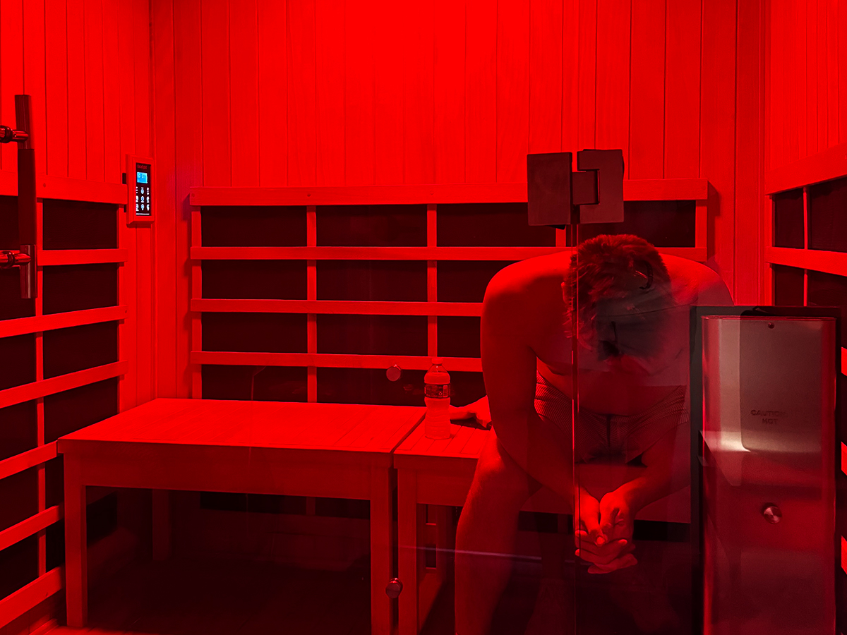 Member seated in the infrared sauna at Beau Monde Elite Fitness under deep red light